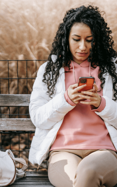 A woman sitting outdoors on a bench checking BCBS coverage for addiction rehab