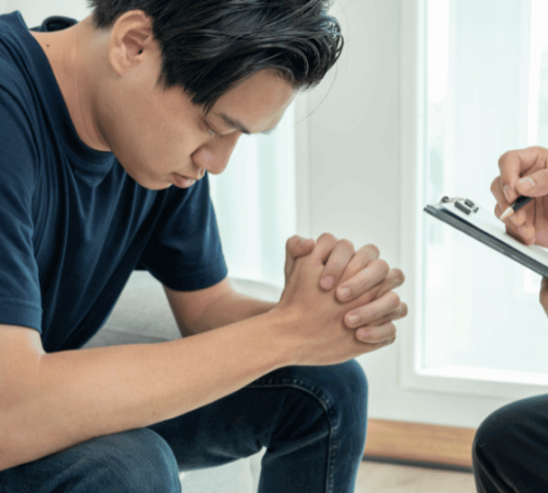 A man with closed eyes meets with a therapist to discuss how insurance coverage for addiction treatment programs