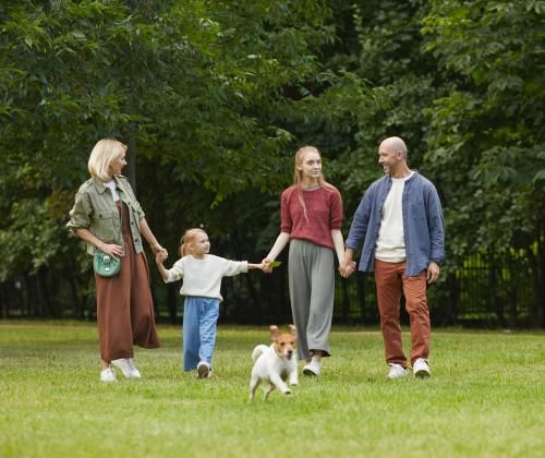 A family walks outdoors as their small dog runs ahead