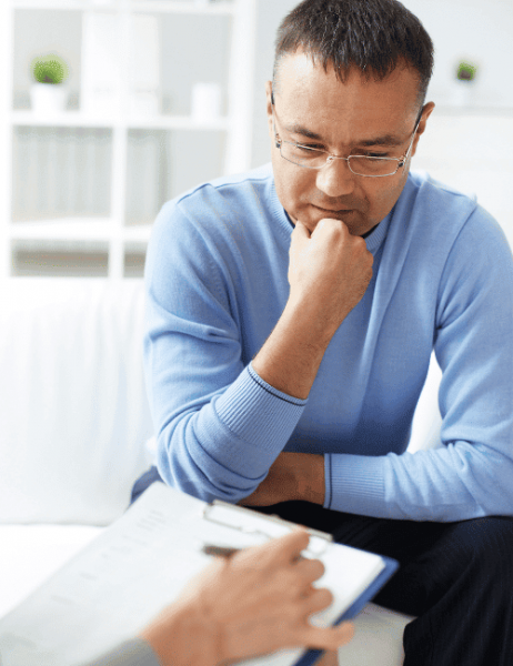 Middle-aged man sitting and thinking while his rehab therapist takes notes