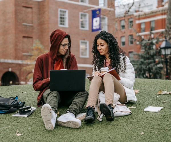 A young male and a young female sitting and studying on the grass of a college campus