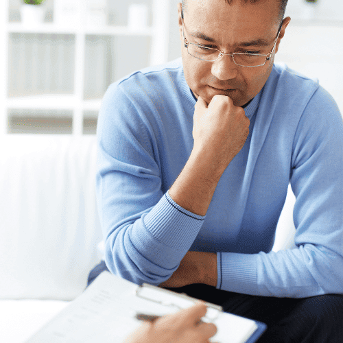 Middle-aged man sitting and thinking while his rehab therapist takes notes